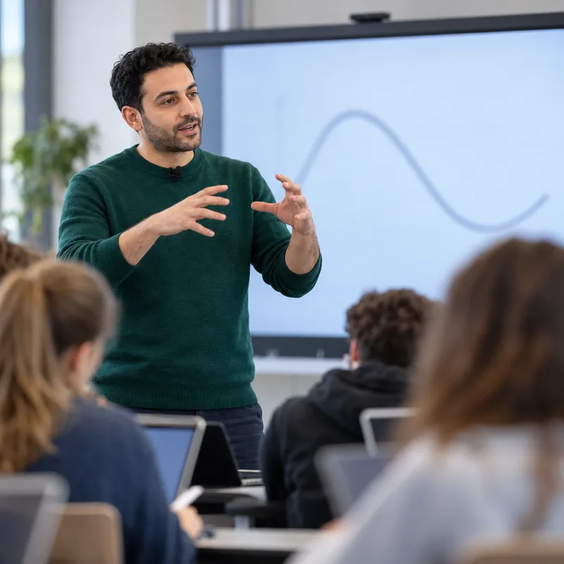 Physics teacher with a clip-on microphone explaining in front of the interactive display