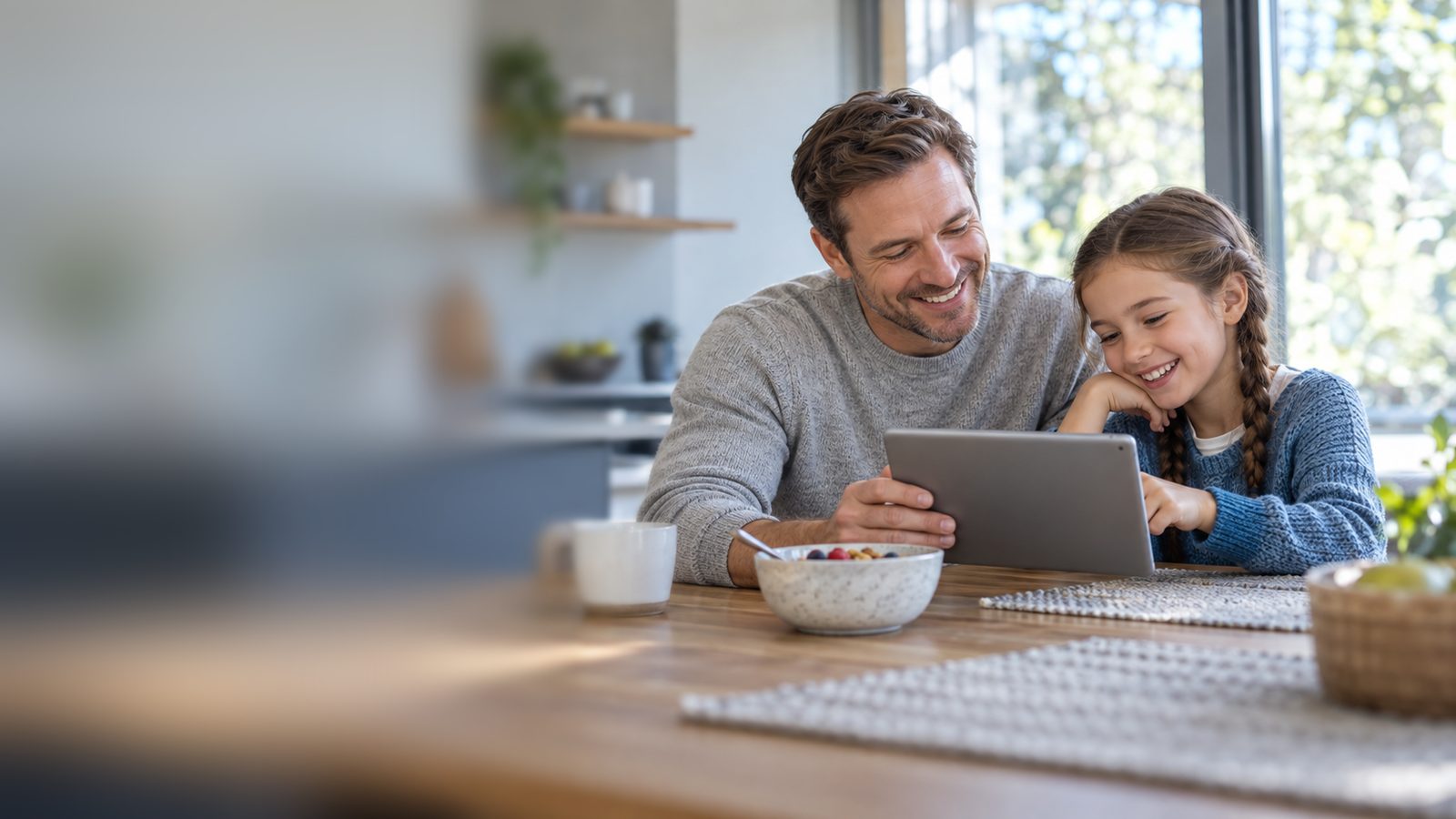 Father and daughter looking at a tablet together at the kitchen table
