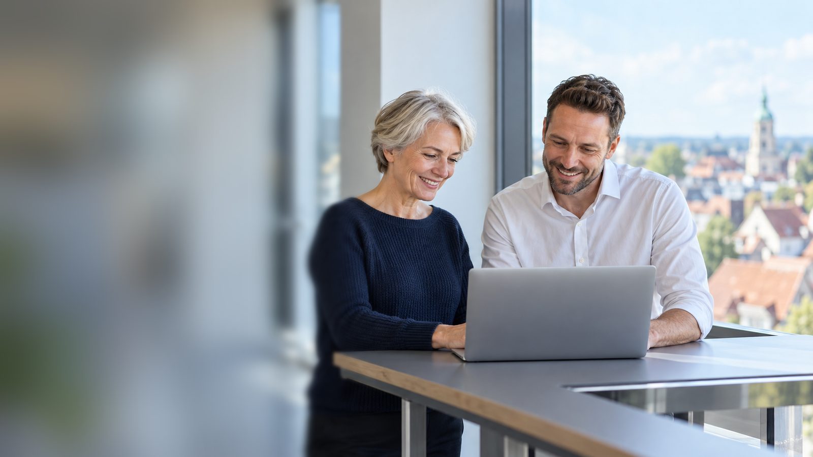 Two staff members of a school authority talk at a laptop with the town in the background